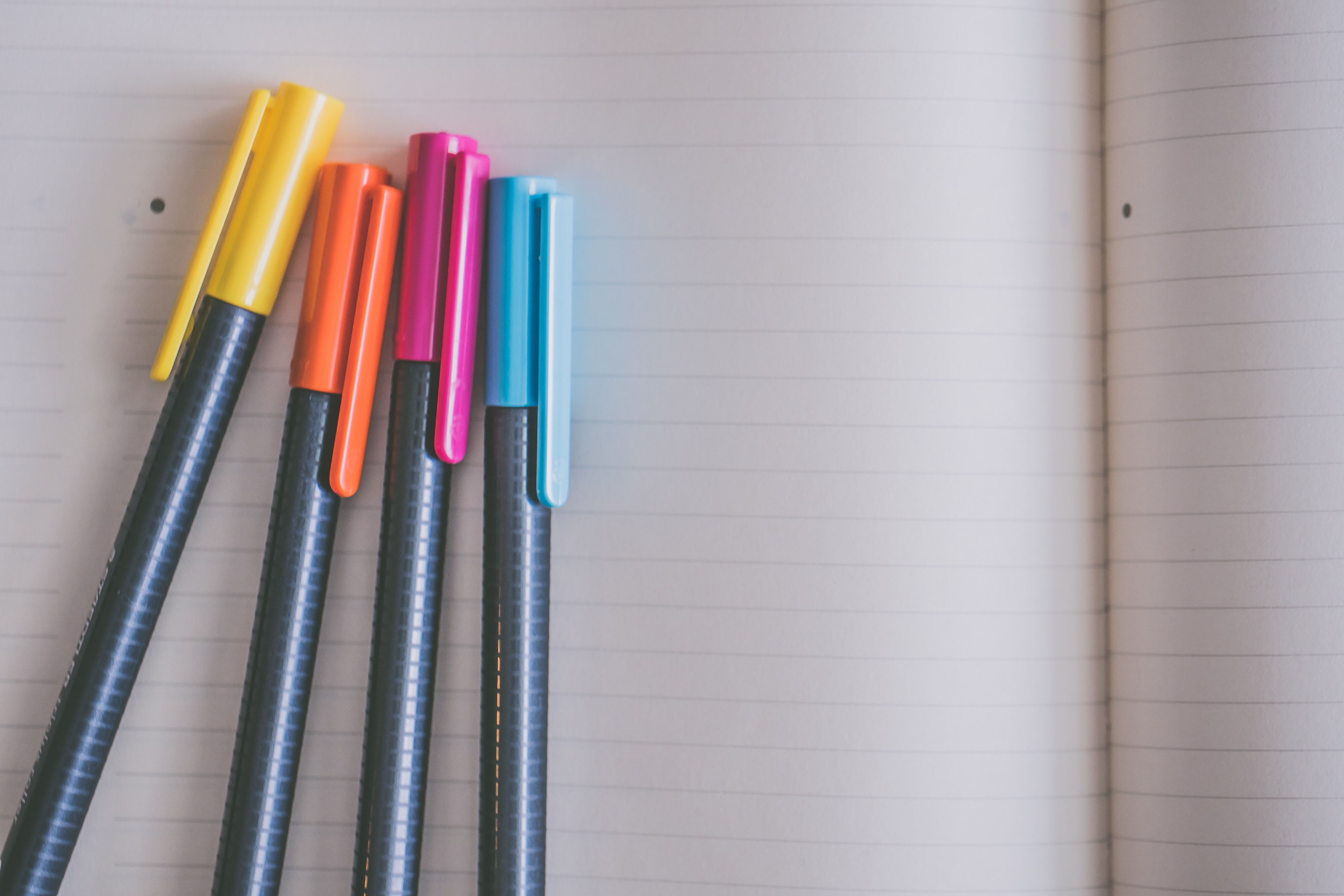 cuatro lápices colores con tapa sobre cuaderno abierto